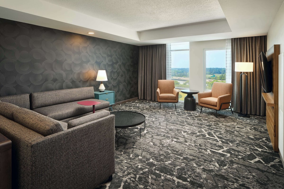 A hotel room with a sofa, two armchairs, a small table, a lamp, and a TV.