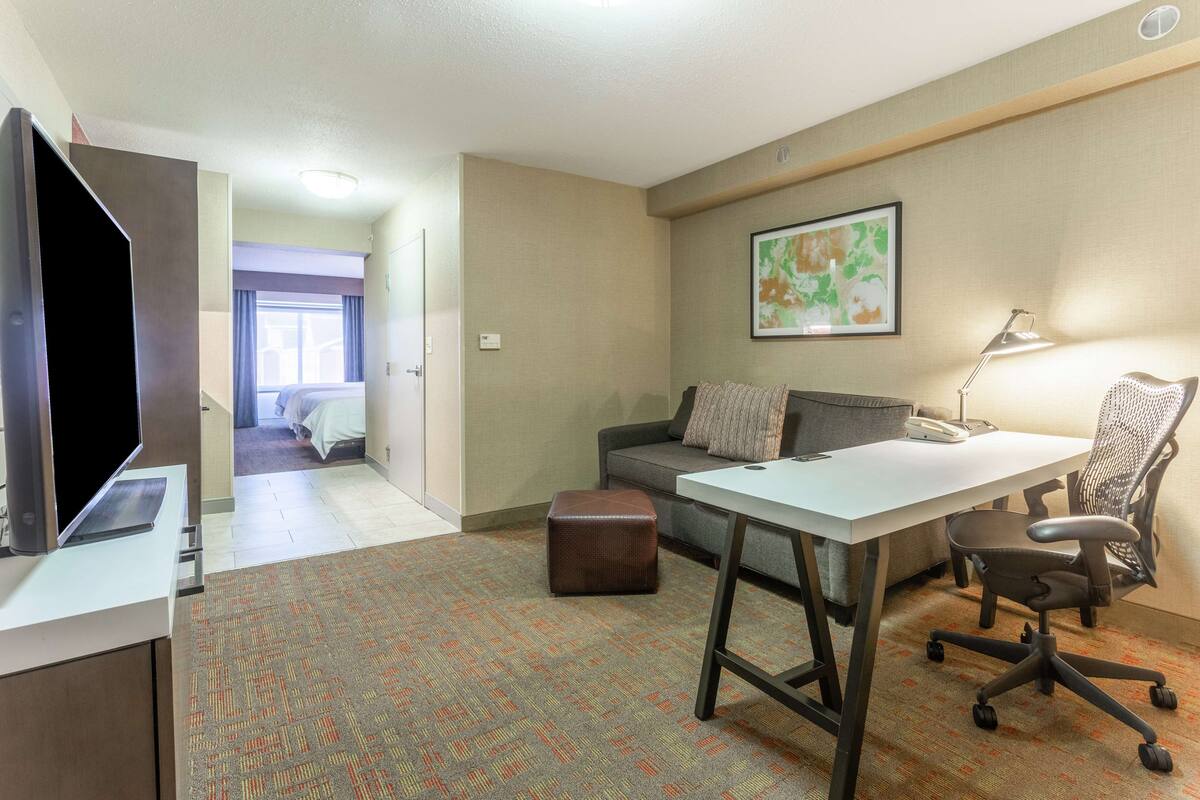 Een hotelkamer met een bureau, bureaustoel en een bed op de achtergrond.