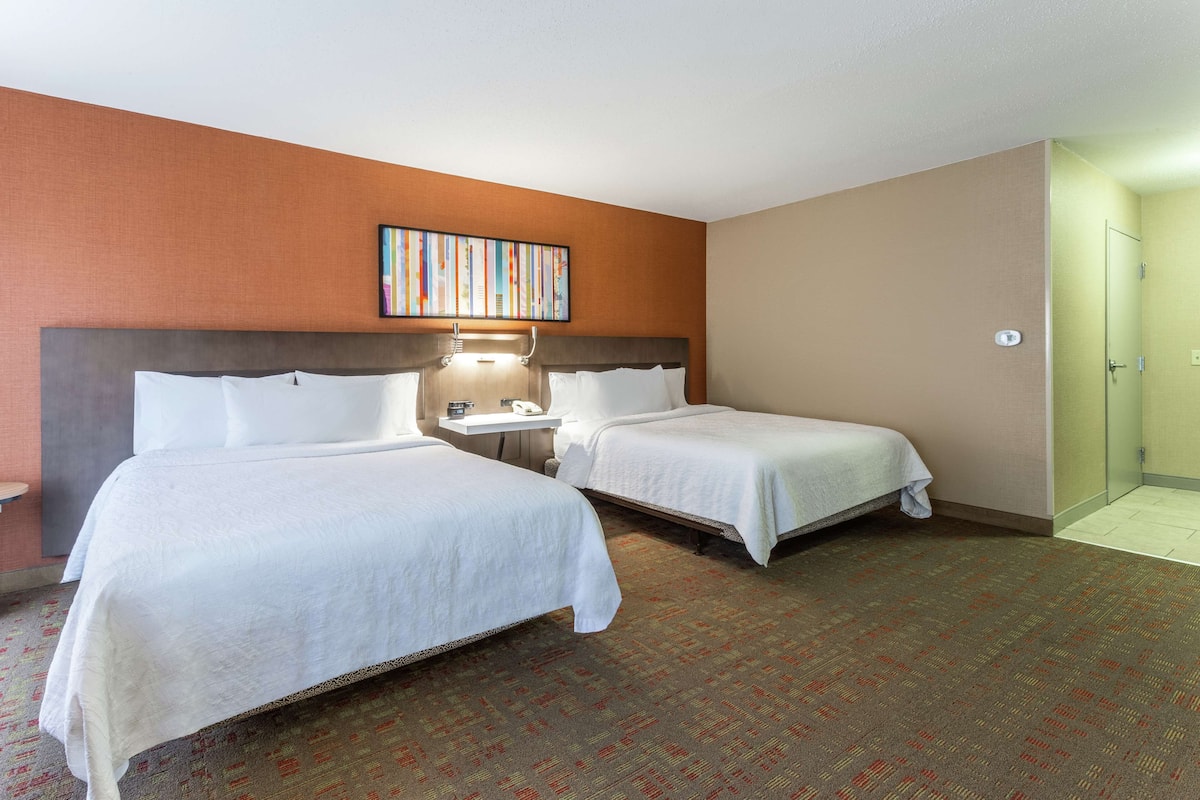 Een hotelkamer met twee bedden, een tafeltje met een lamp en een schilderij aan de muur.