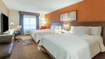 A hotel room with two beds, a desk with a computer, a TV, and a window with curtains.