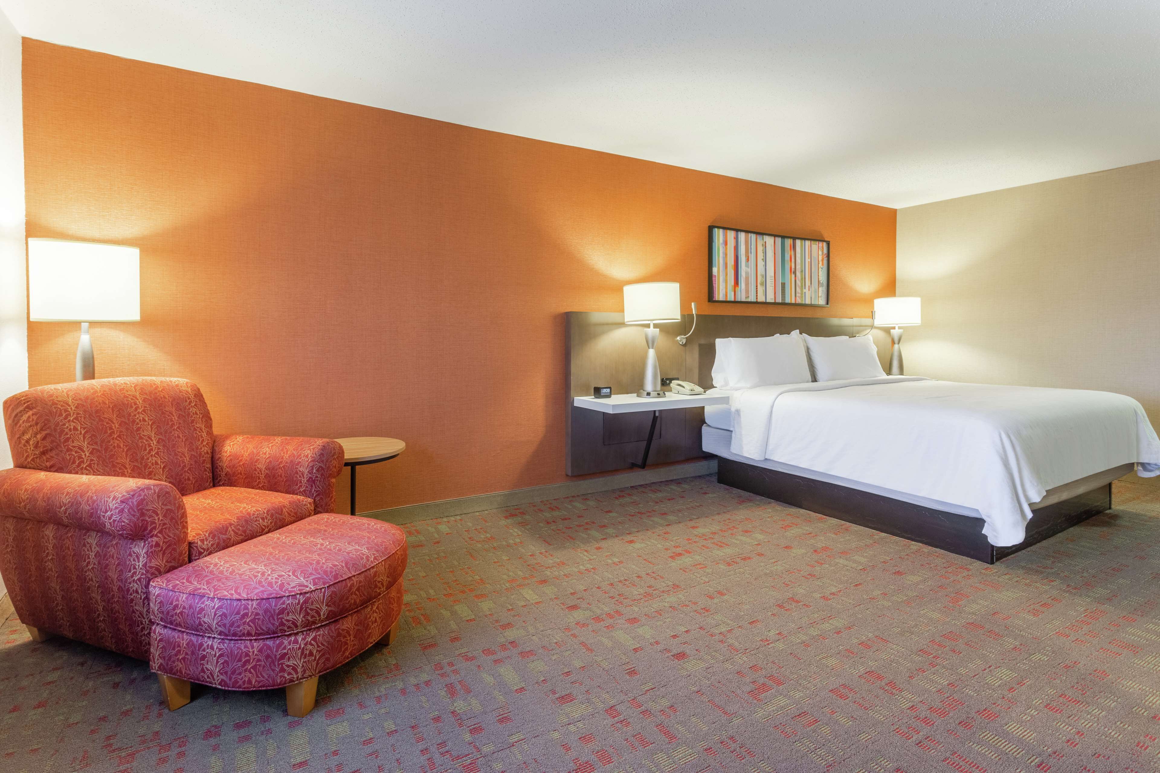 A hotel room with a bed, two bedside tables, a chair, and a small table.