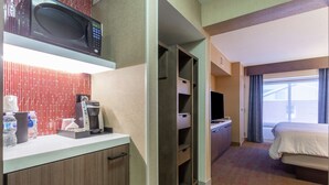 Een hotelkamer met een kitchenette, een bed, een televisie en een raam met gordijnen.