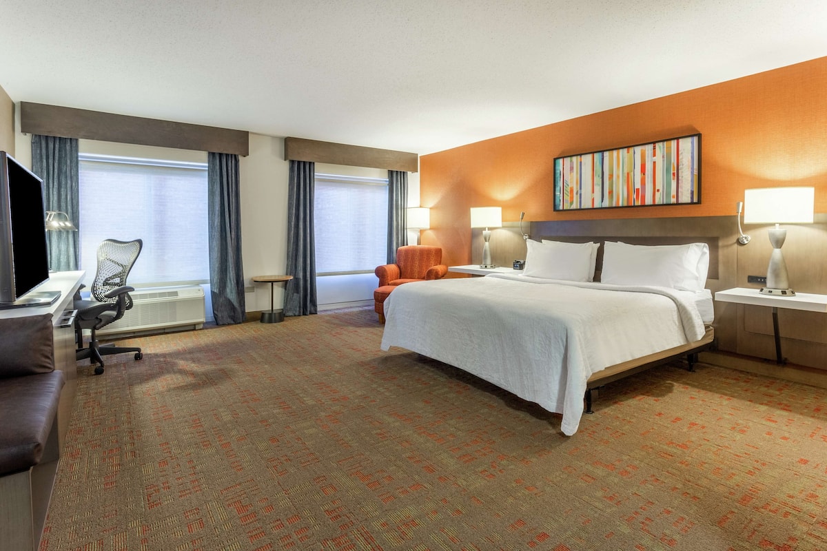 Een hotelkamer met een groot bed, een bureau met stoel, een televisie en twee lampen.