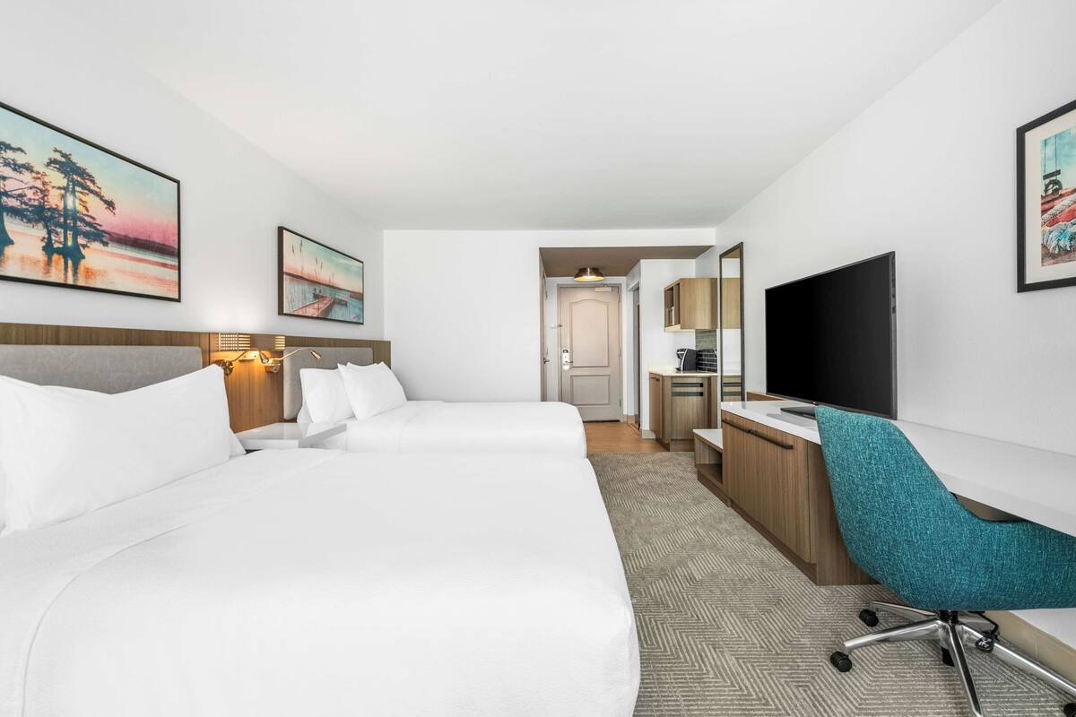 A hotel room with a large bed, a desk, a chair, a TV, and artwork on the walls.