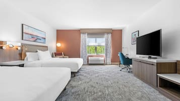 Quarto de hotel com duas camas, uma escrivaninha, televisão e uma janela grande com cortinas.
