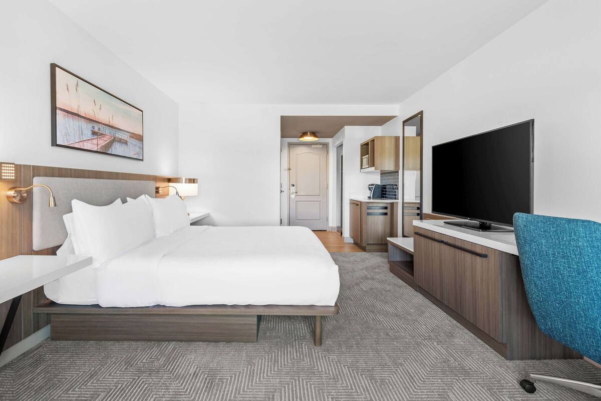 A hotel room with a bed, a desk, a TV, and a kitchenette.
