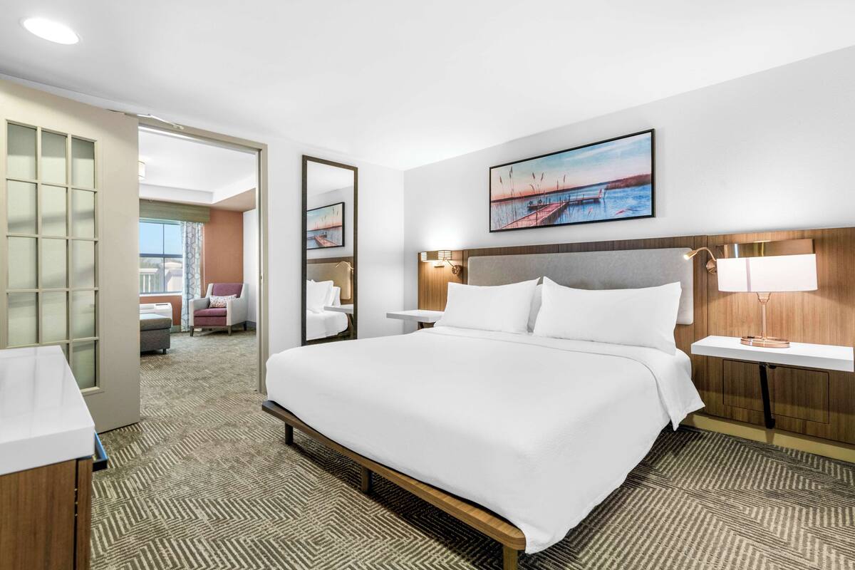 A hotel room with a large bed, a bedside table with a lamp, a mirror, and a painting on the wall.