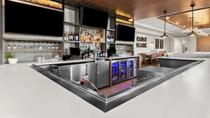 A modern bar area with stainless steel appliances, a wine rack, and a seating area with a wooden ceiling. - Hilton Garden Inn Suffolk Riverfront (Suffolk)