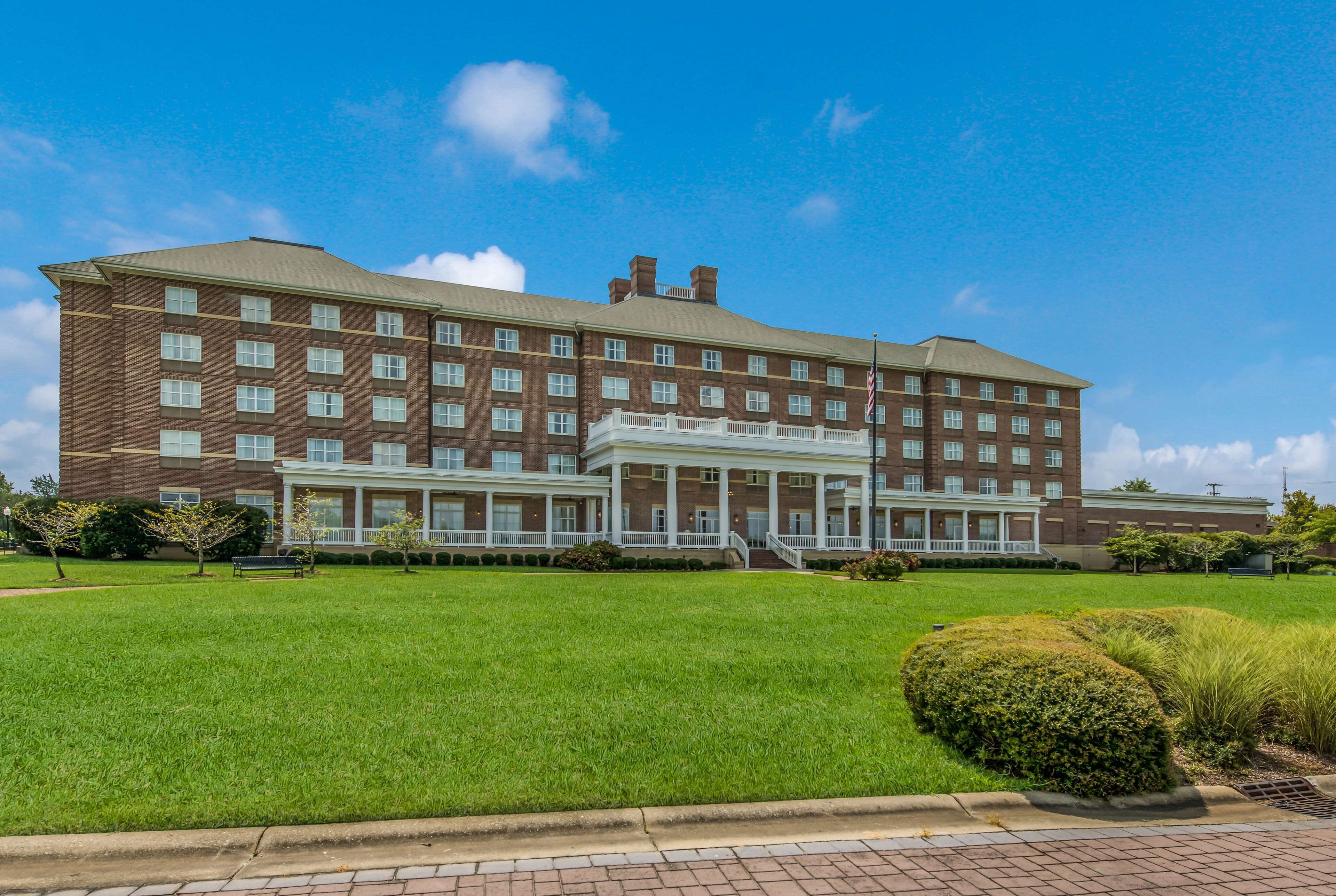 A large brick building with a central entrance, multiple windows, and a well-maintained lawn.