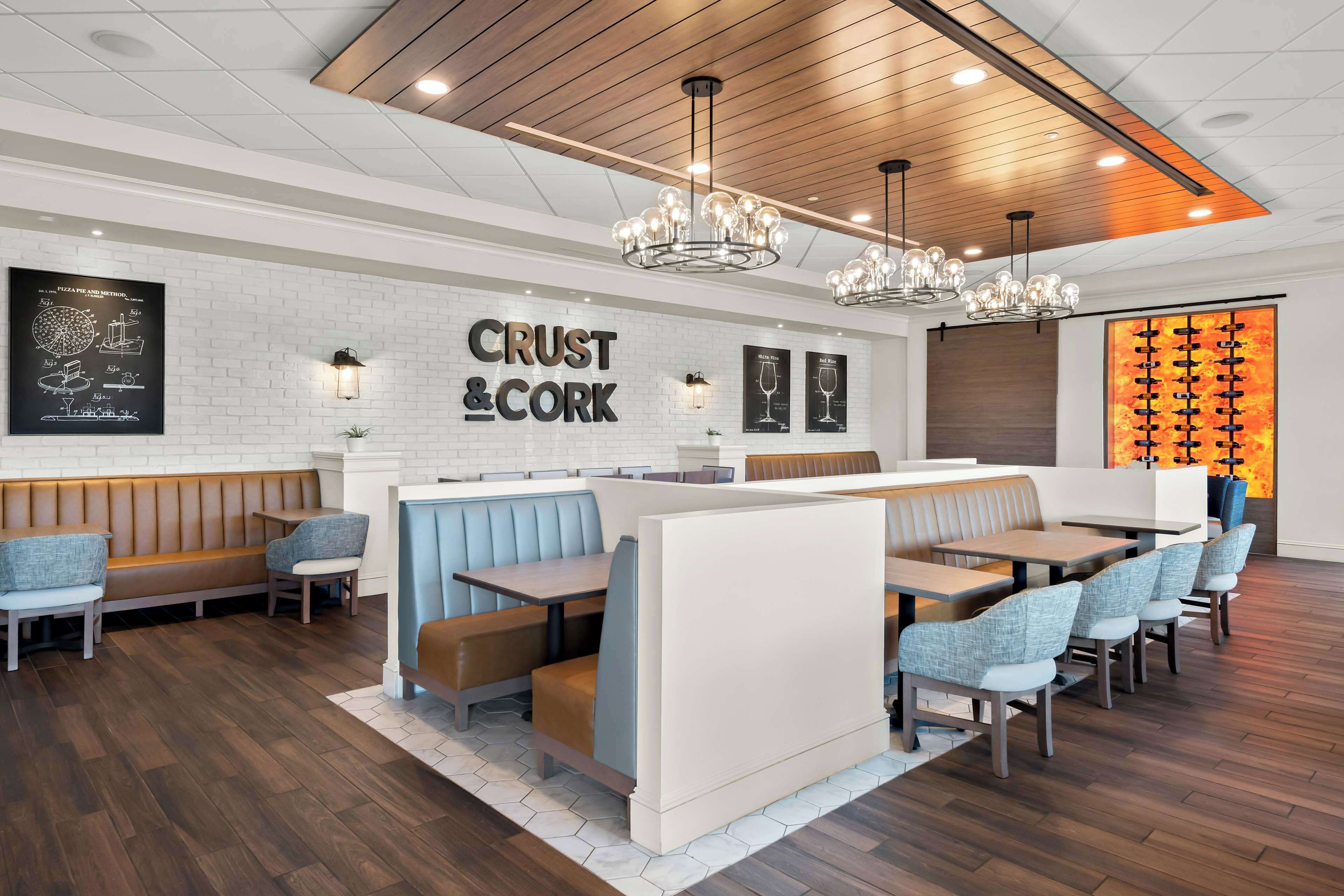 Een restaurantinterieur met een witte bakstenen muur, houten plafond en moderne verlichtingsarmaturen.