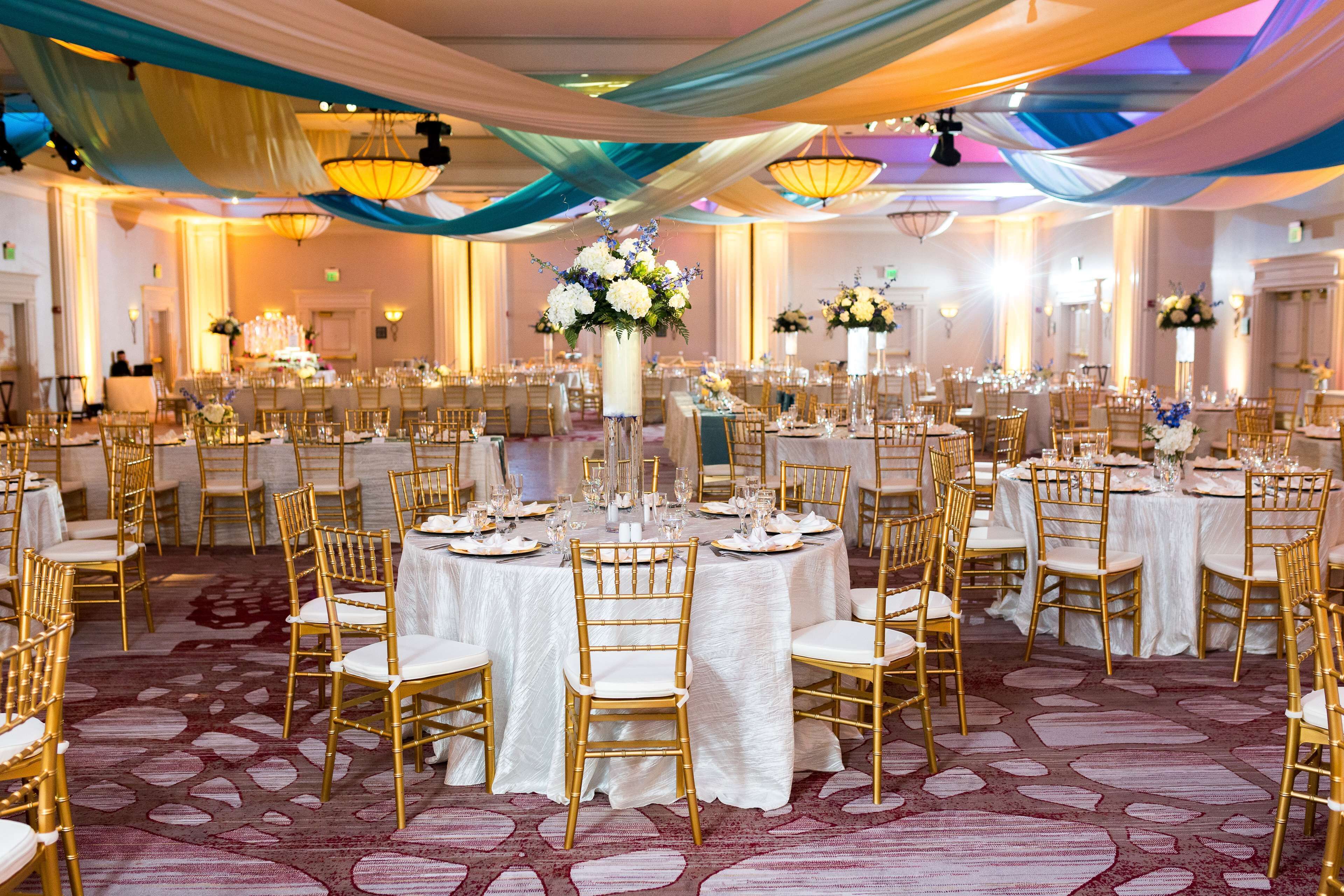 A banquet hall with round tables, gold chairs, and white tablecloths.