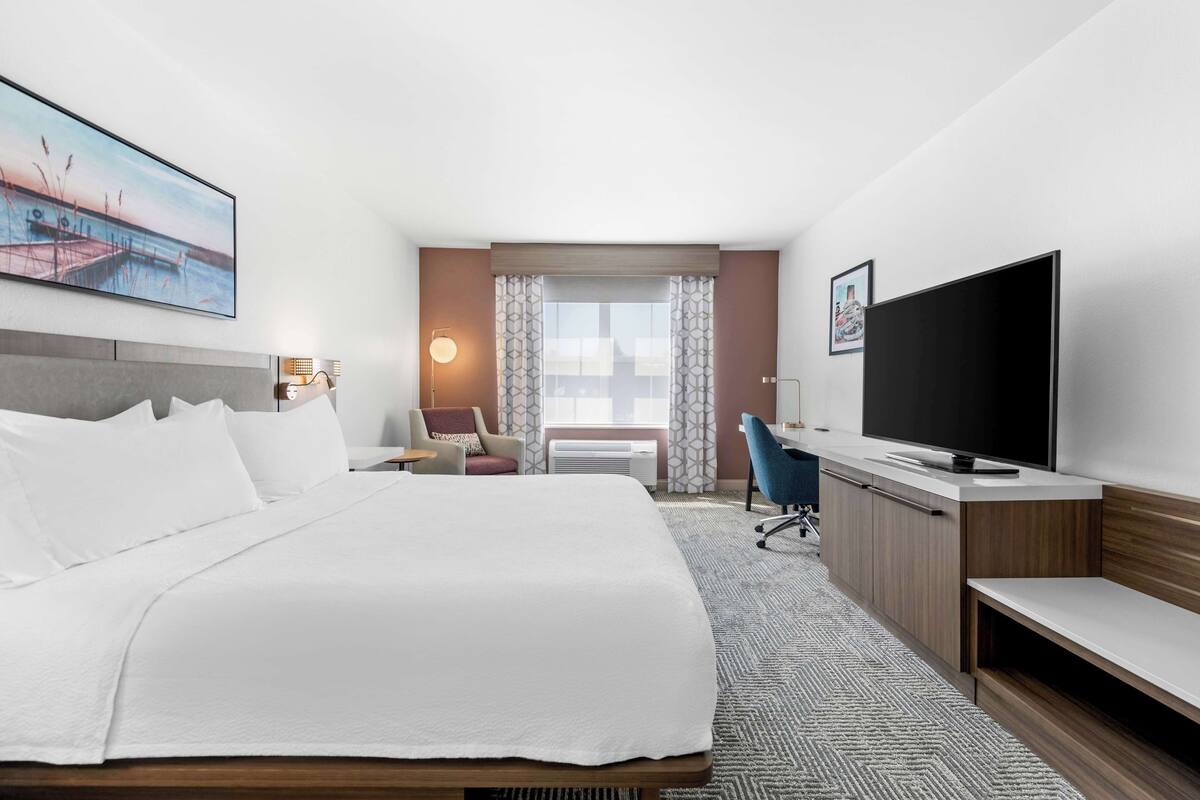 A hotel room with a large bed, a desk, a chair, a TV, and a window with curtains.
