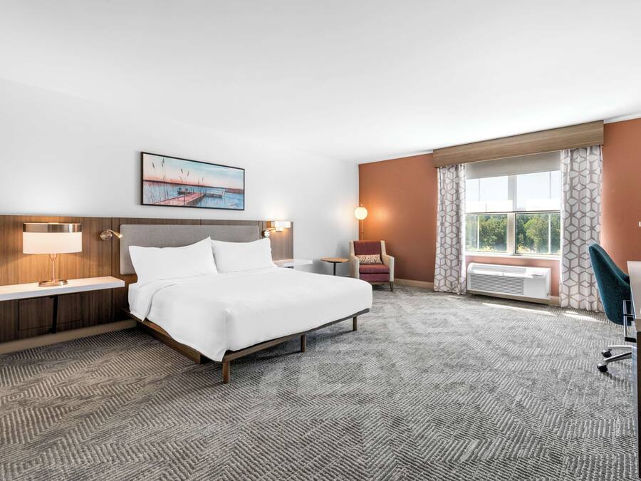 Une chambre d’hôtel avec un grand lit, un bureau, une chaise, une petite table et une fenêtre avec des rideaux.