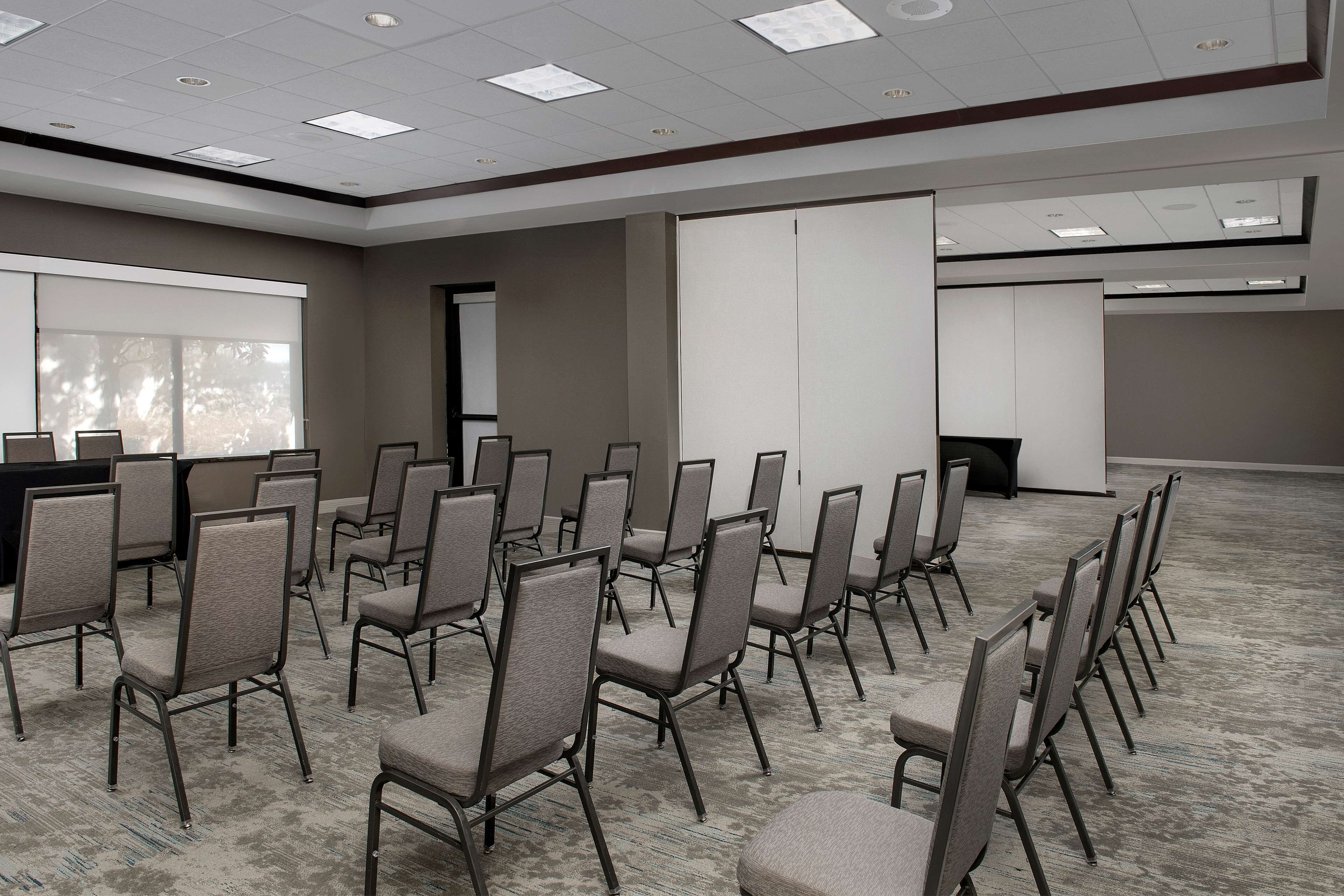 A conference room with rows of chairs, a projector screen, and a large window with a view of trees.