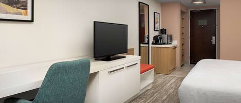 A hotel room with a bed, a desk with a television, a chair, and a coffee machine.