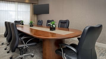 A conference room with a large wooden table, black leather chairs, and a flat-screen TV on the wall.