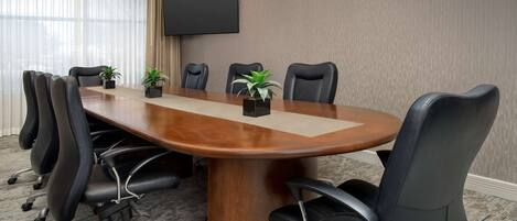 Une salle de conférence avec une grande table en bois, des fauteuils en cuir noir et un téléviseur à écran plat fixé au mur.