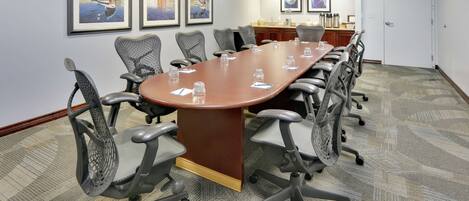 A conference room with a long table, multiple chairs, framed artwork on the walls, and a door in the background.
