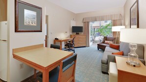 A hotel room with a wooden desk, a sofa, a television, and a balcony with a view.