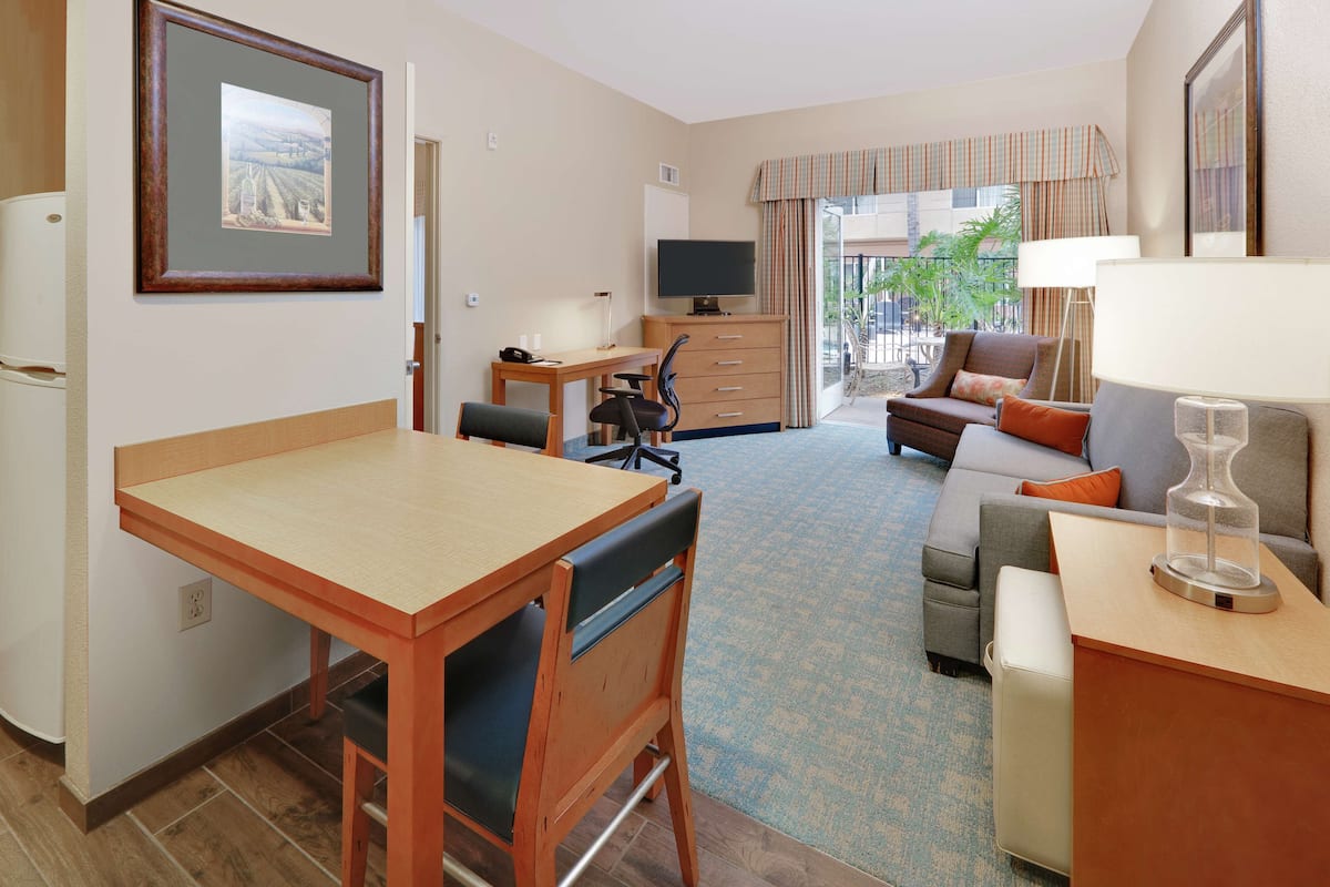 A hotel room with a wooden desk, a sofa, a television, and a balcony with a view.