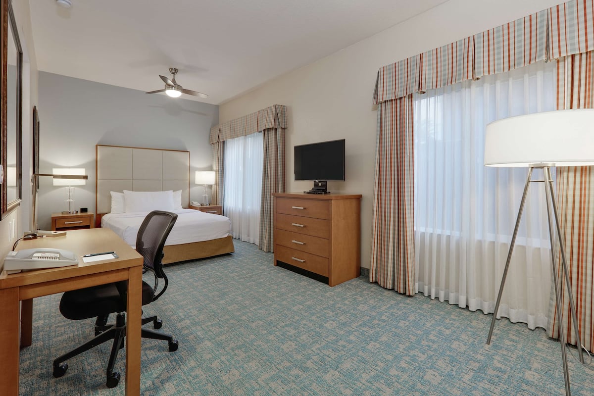 A hotel room with a bed, desk, chair, TV, dresser, and curtains.