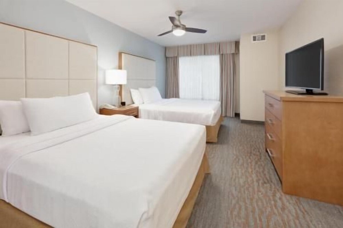 A hotel room with two beds, a TV, a ceiling fan, and a wooden dresser.