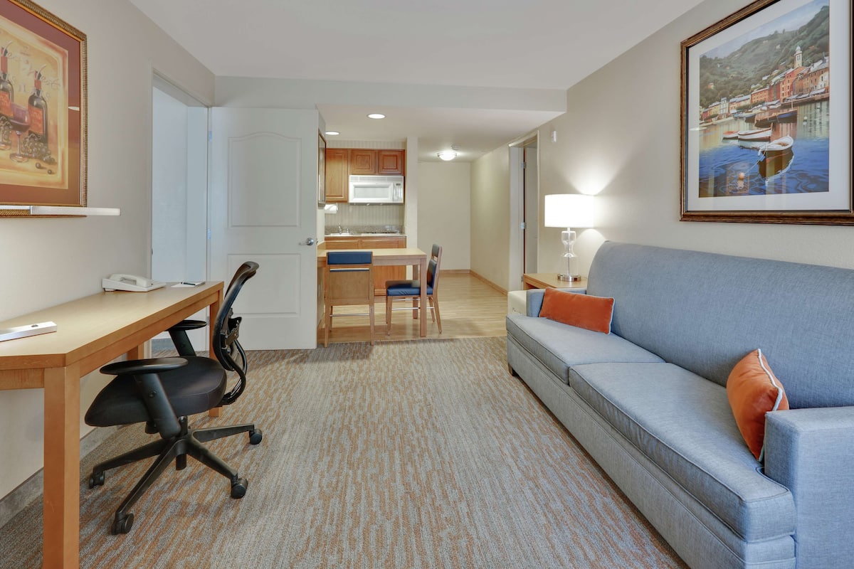 A hotel room with a kitchenette, a sofa, a desk, and a chair.