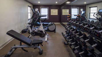Un gimnasio con equipo de cardio, mancuernas y una banca.