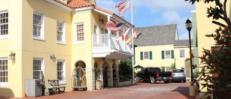 A yellow building with a red-tiled roof, a balcony with American flags, and a paved courtyard.