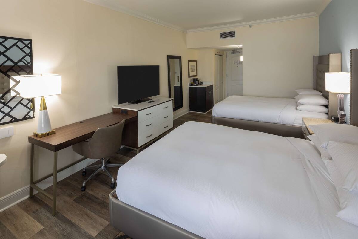 Ett hotellrum med två sängar, ett skrivbord med en stol, en tv, en spegel och en garderob.