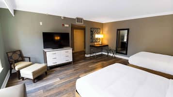 A hotel room with a large bed, a TV, a desk with a lamp, a chair, and a wardrobe.