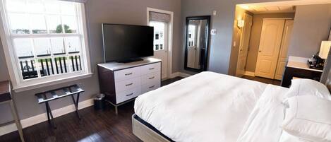 A bedroom with a bed, a TV on a dresser, a window with a view, and a door leading to another room.
