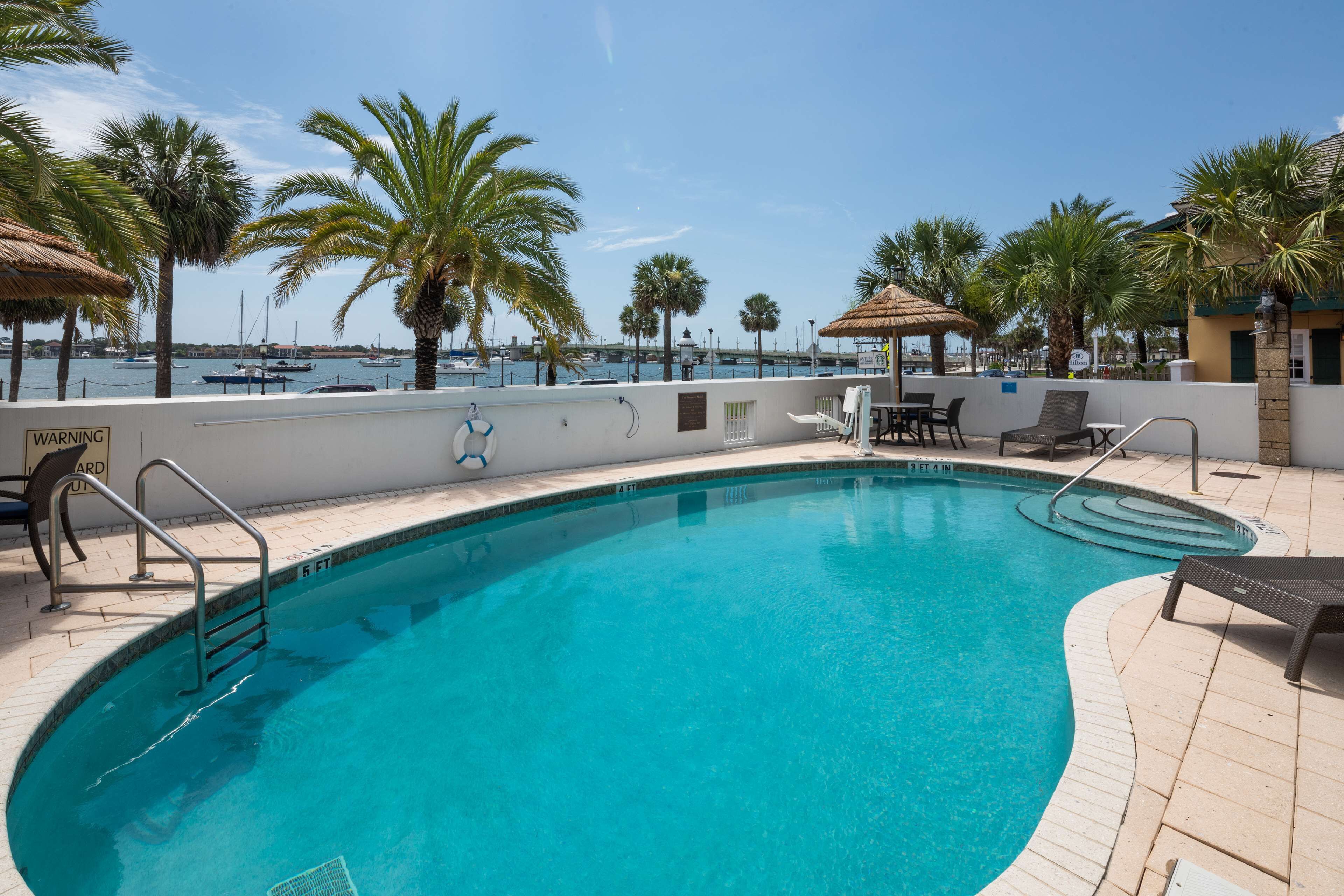 A swimming pool with a safety railing, lounge chairs, and palm trees.