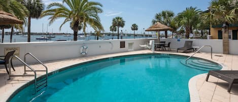 A swimming pool with a safety railing, lounge chairs, and palm trees.