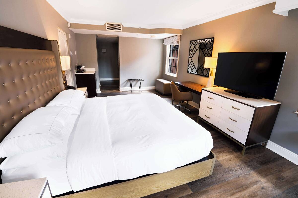 Ett modernt hotellrum med en stor säng, ett skrivbord med en platt-TV och en stol.