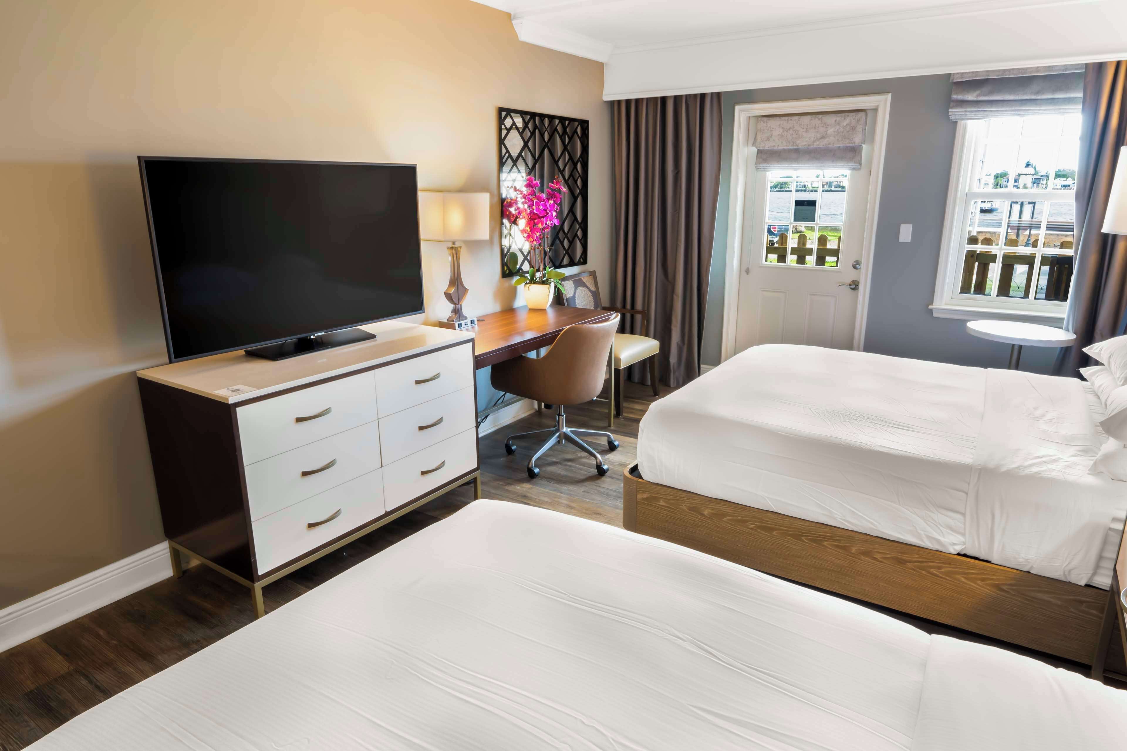 A hotel room with two beds, a desk with a TV, a chair, and a window with a view.