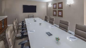 A conference room with a long table, chairs, a flat-screen TV, framed pictures, and a small vase with colorful items.