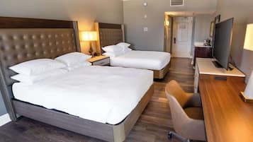 A hotel room with two beds, a desk, a chair, a TV, and a lamp.
