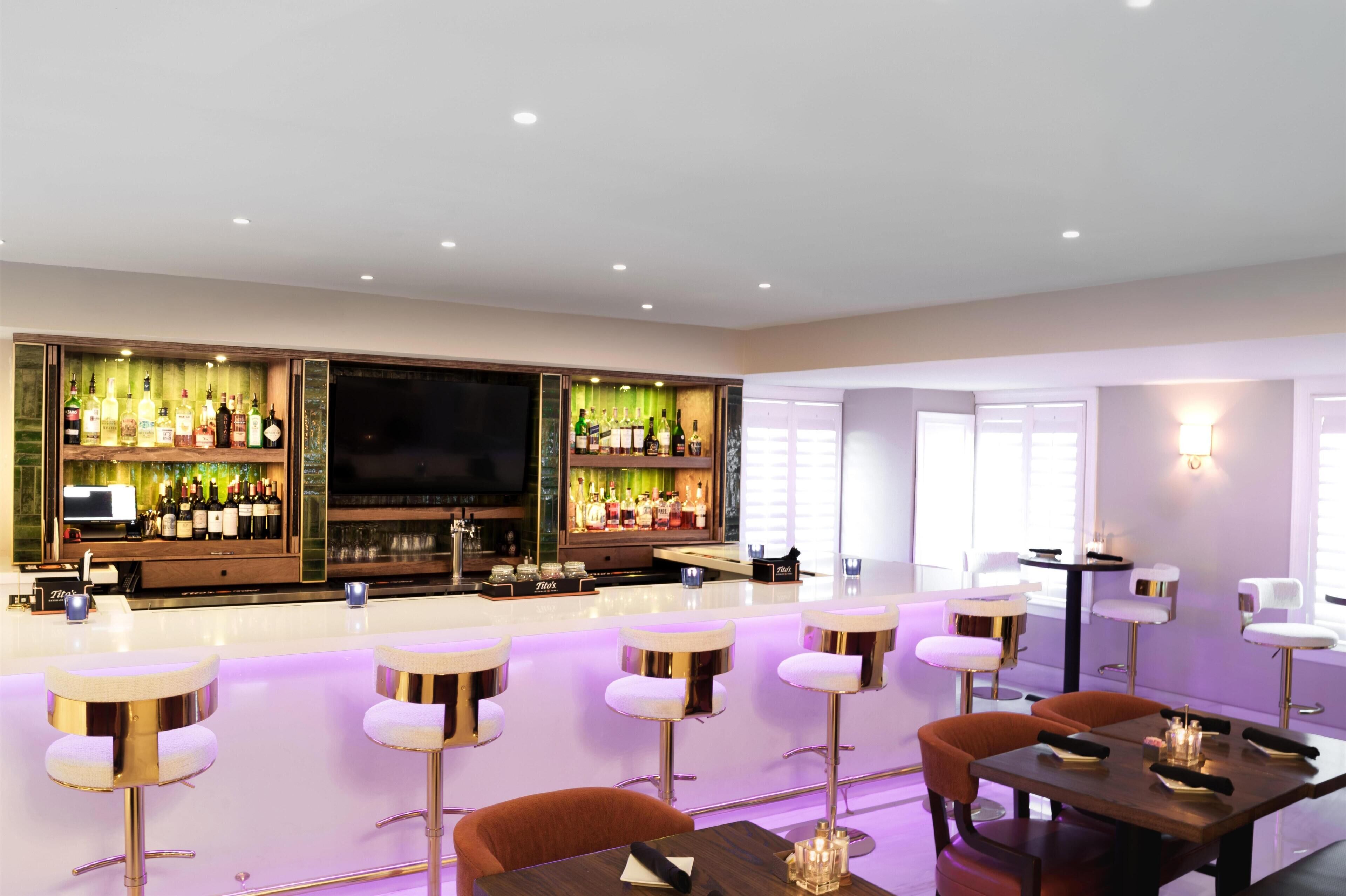 A bar area with multiple stools, a television, and a bar stocked with bottles.
