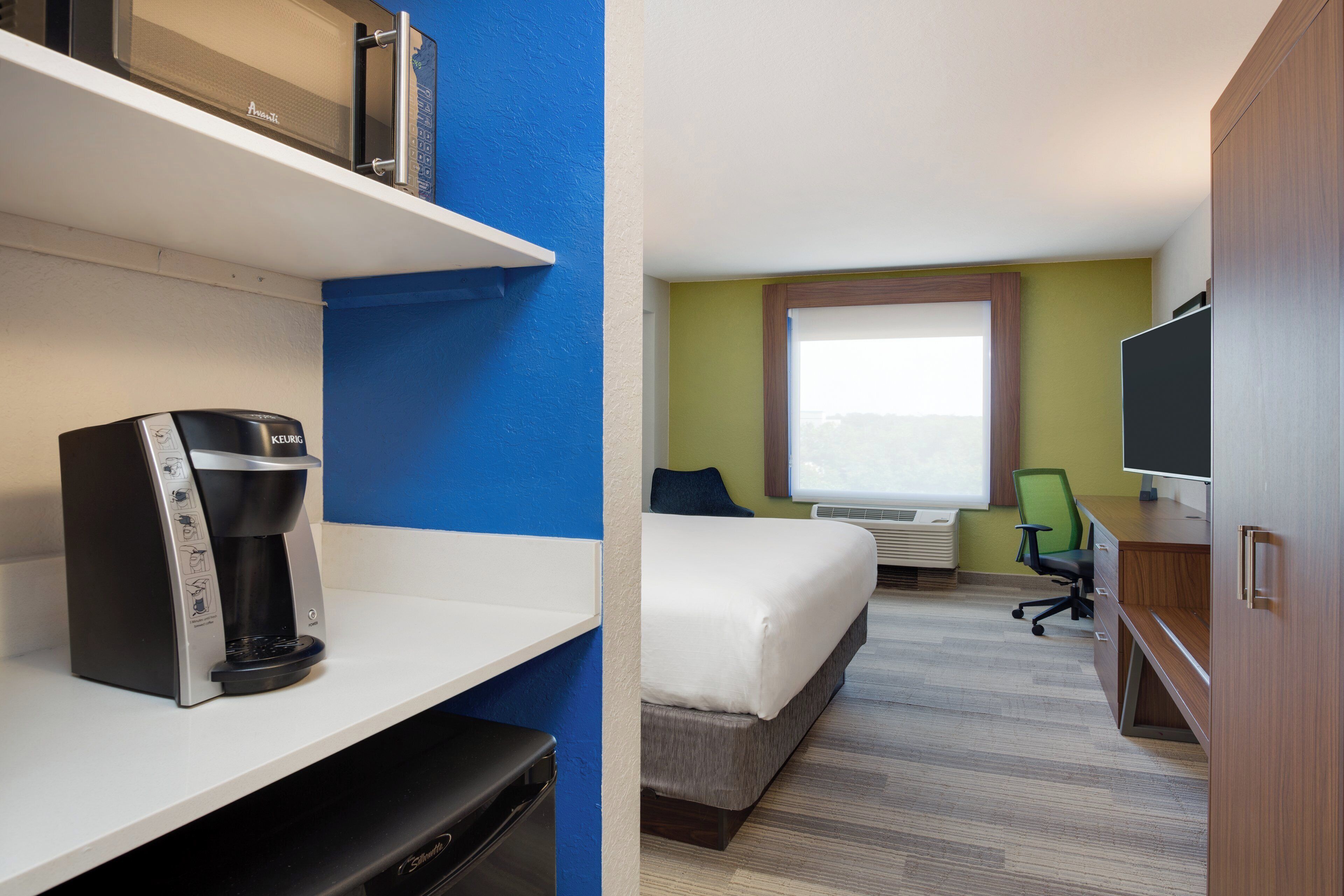 A hotel room with a bed, a desk with a computer, a coffee maker, and a television.