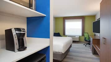 A hotel room with a bed, a desk with a computer, a coffee maker, and a television.
