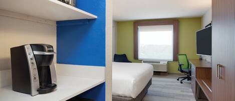 A hotel room with a bed, a desk with a computer, a coffee maker, and a television.