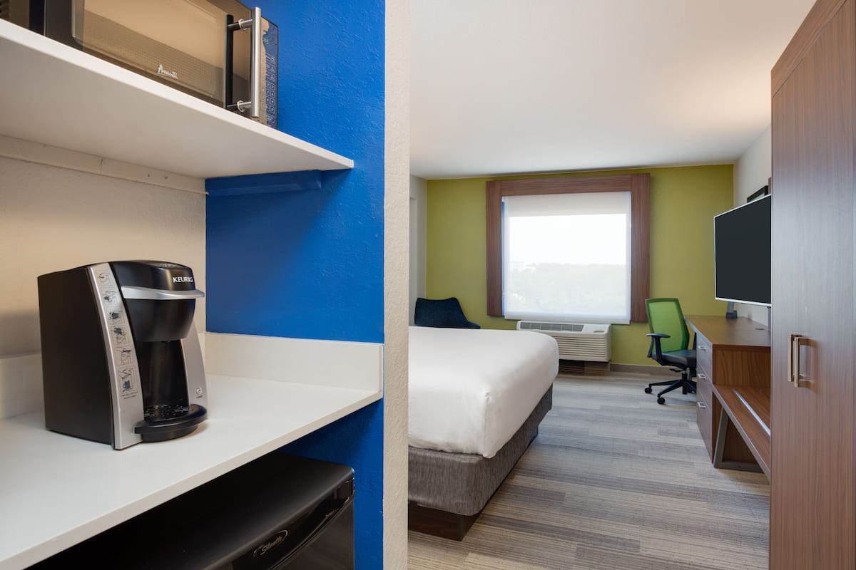A hotel room with a bed, a desk with a computer, a coffee maker, and a television.