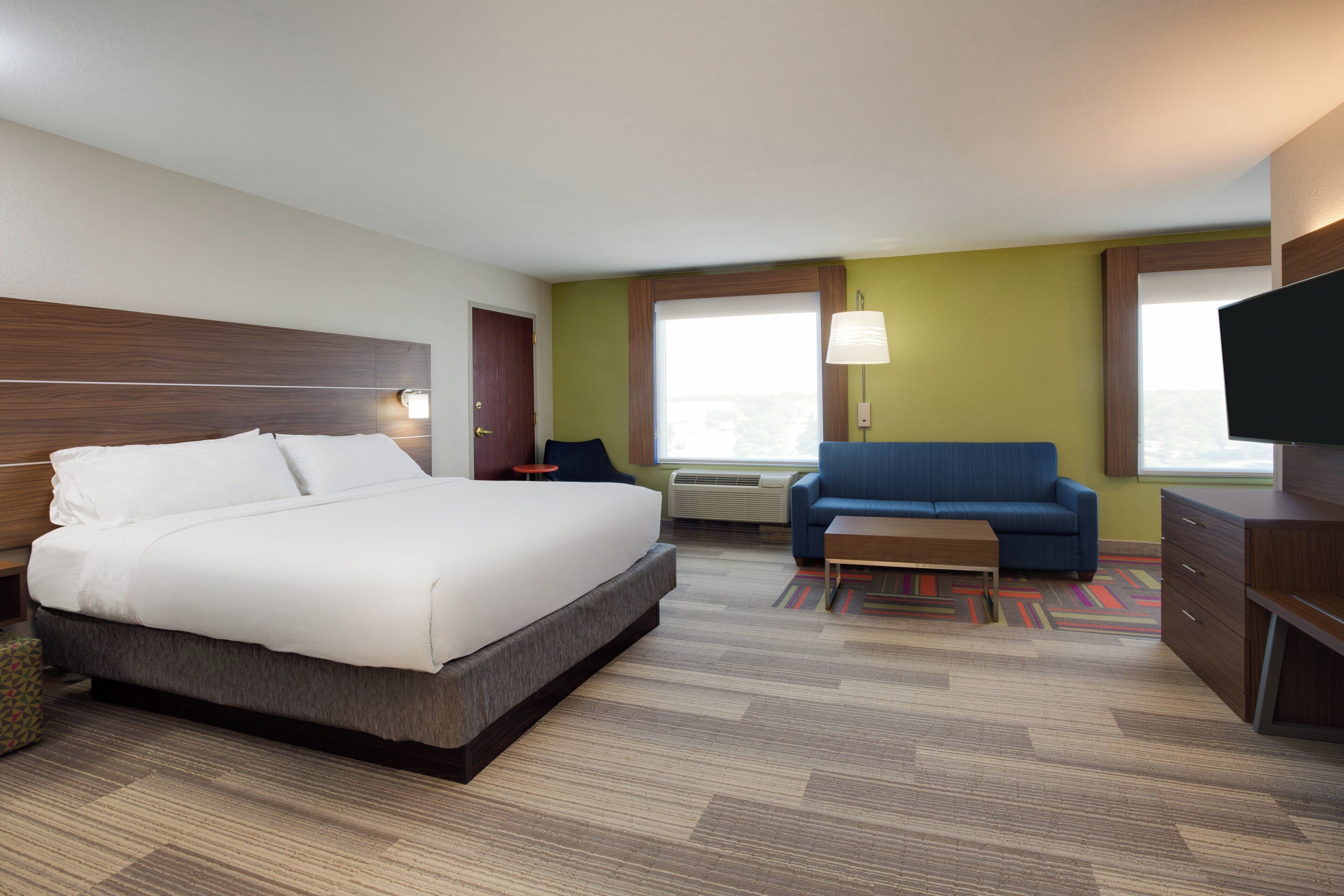 Een hotelkamer met een bed, een blauwe bank, een klein tafeltje, een televisie en een raam.