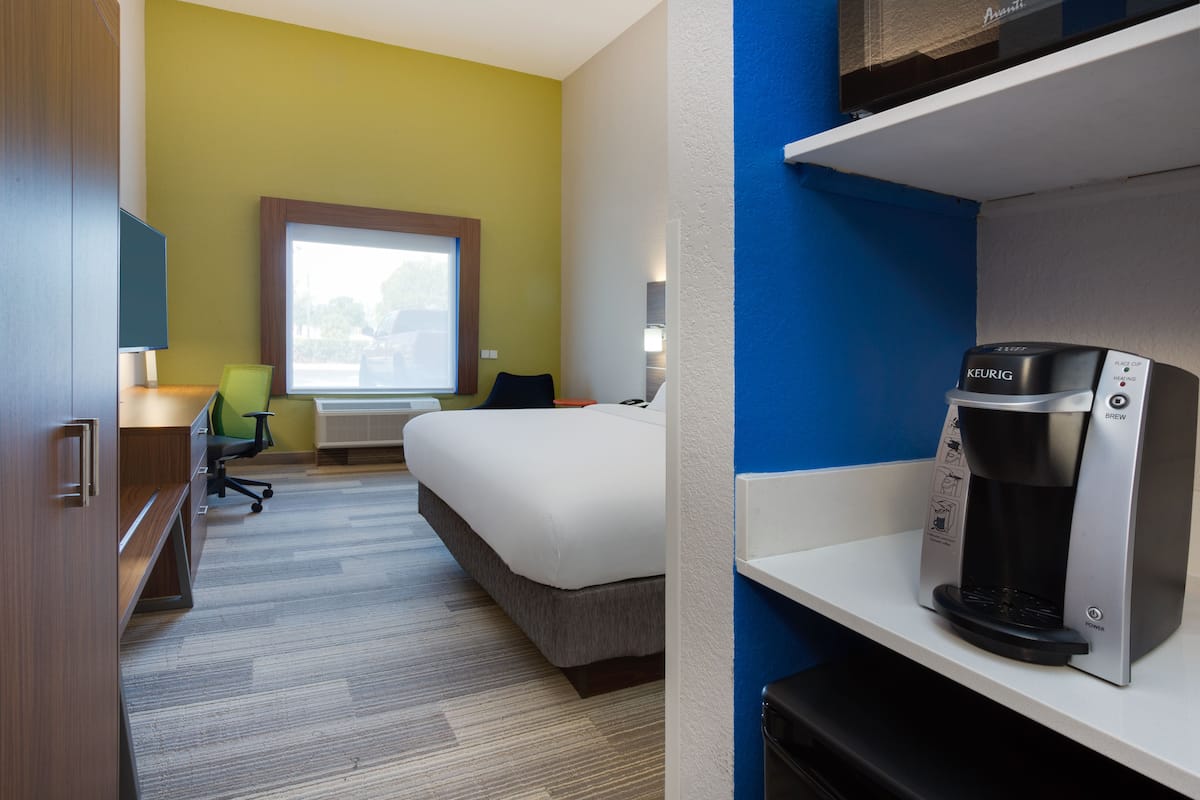 A hotel room with a bed, desk, chair, coffee maker, and a window with a view.