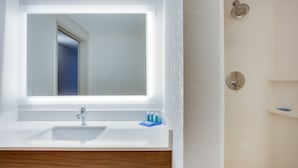 Un baño con lavamanos blanco, espejo y ducha.