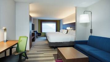 A hotel room with a bed, a desk, a chair, a sofa, and a lamp.