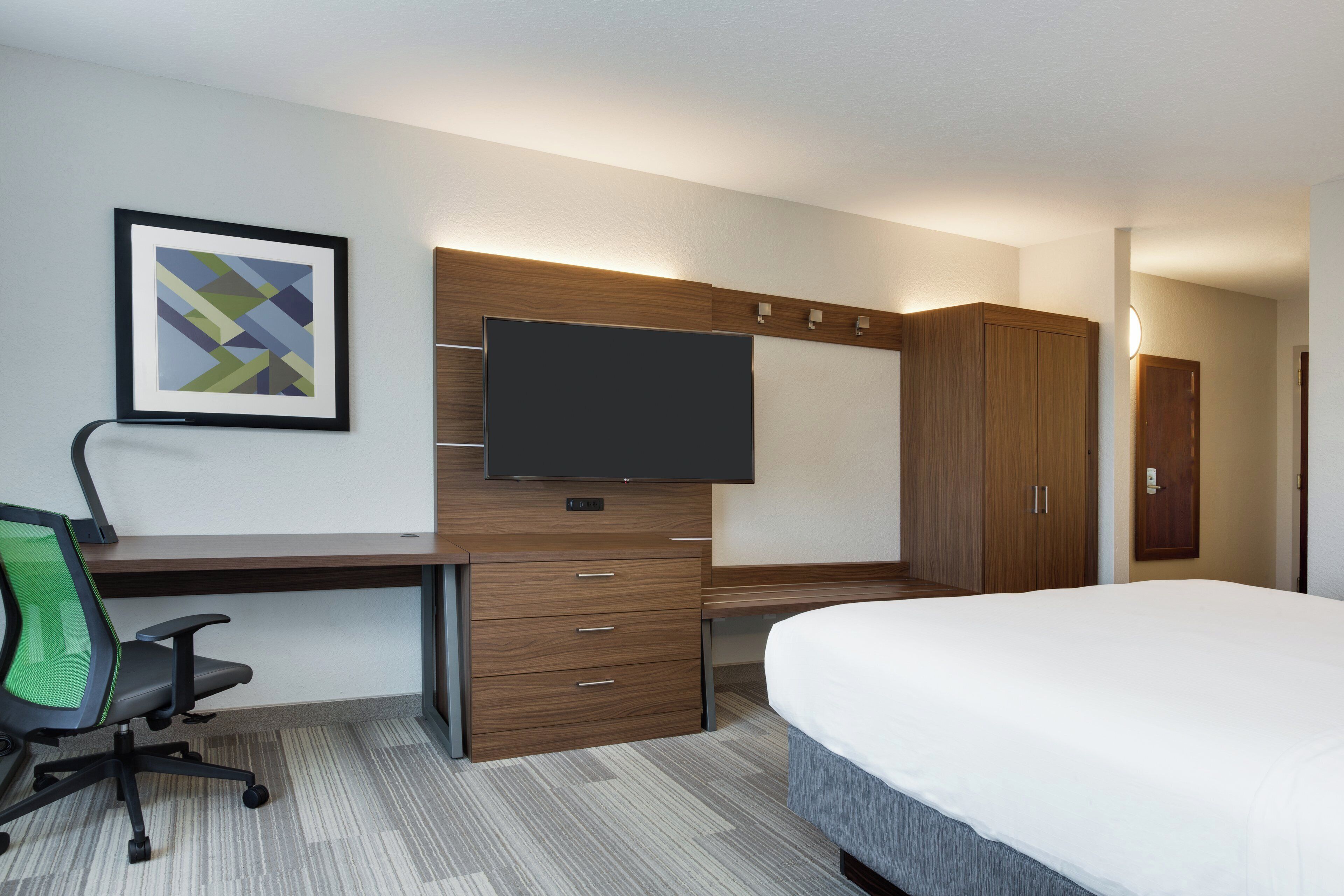 Een hotelkamer met een bed, een bureau met stoel, een televisie en een kledingkast.