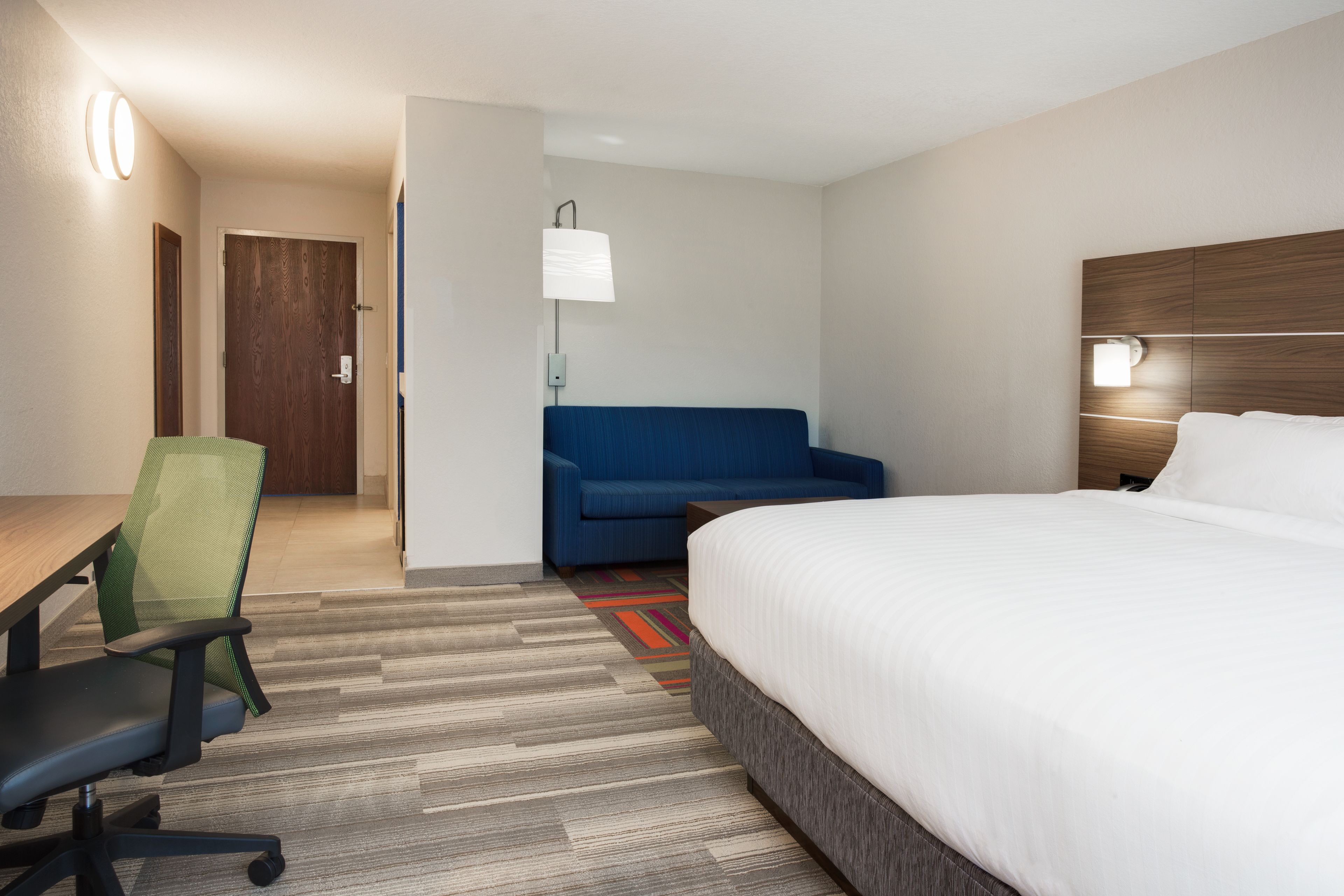 A hotel room with a bed, a desk, a chair, a sofa, and a lamp.