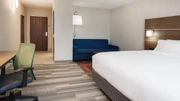 A hotel room with a bed, a desk, a chair, a sofa, and a lamp.